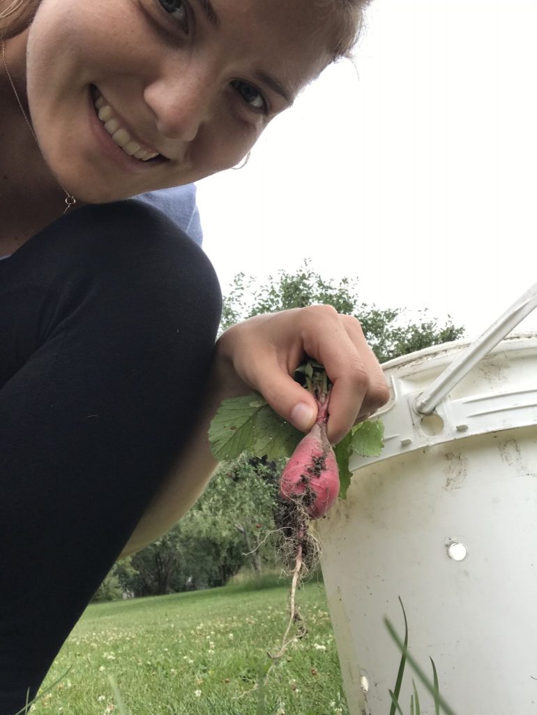 Adeline souriante tiens un radis rouge dans ses mains.